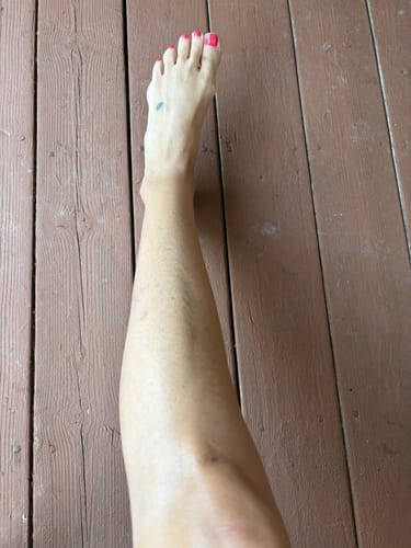Reviewer's leg with a radiant summer glow after applying Body Serum - Summer Glow, against a wooden background.