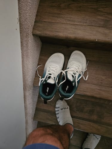 Customer's pair of CUURT Muuv court shoes in white and dark green sitting on wooden stairs.
