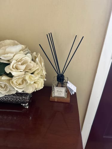 Customer's Istanbul Reed Diffuser with black reeds in a square glass bottle, sitting beside a bouquet of white roses.