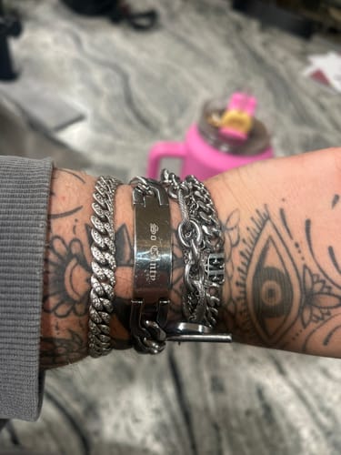 Reviewer's wrist wearing the stainless steel Cuban link ID bracelet with personalized engraving alongside other jewelry.