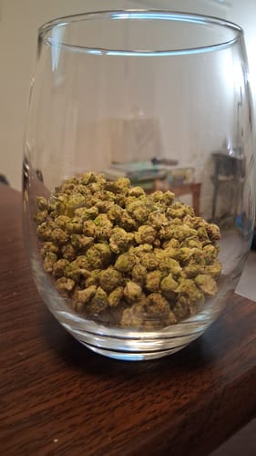 Customer's 1 Oz Cheap THCA Small Buds in a clear glass on a wooden surface.
