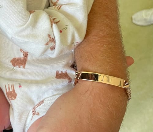 Customer's shiny rose gold Cuban link bracelet worn on a person's wrist next to an infant in patterned clothing.
