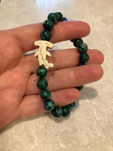 Customer's Shark Week Bracelet with dark blue and green stone beads and a white hammerhead charm held in a hand.