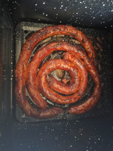 Reviewer's Air Fryer Novio StonePro holding a large, browned coiled sausage in the cooking basket.