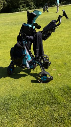 Customer's Cybercart golf cart with a teal and black bag on a sunny grassy course.