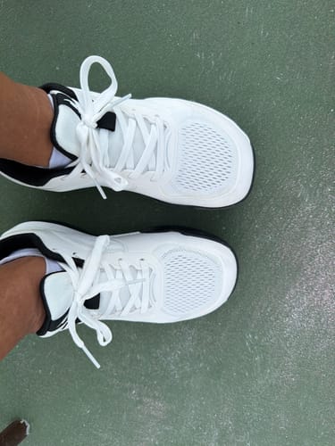 Customer's white CUURT Muuv court shoes with a wide toe box, worn on feet over a green court surface.