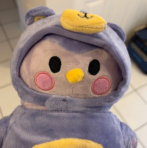 Customer's Mini Finch Plushie in a soft purple bear costume with yellow accents, close-up shot.