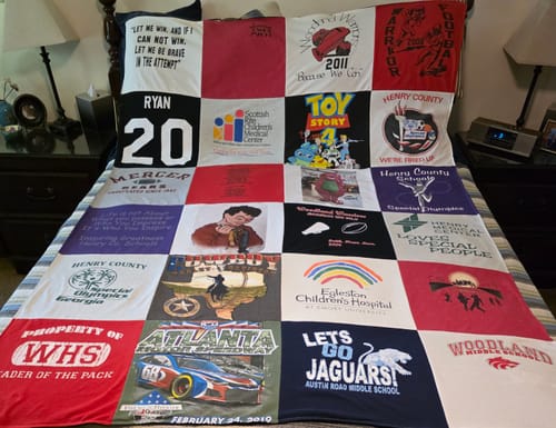 Customer's Project Repat T-Shirt Quilt displayed on a bed, showing various colorful shirt graphics.