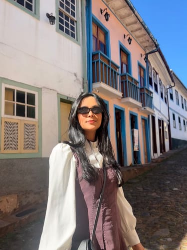 Customer's Óculos de Sol Cumbuco em uso, com design ovalado e retrô, em uma rua histórica ensolarada.