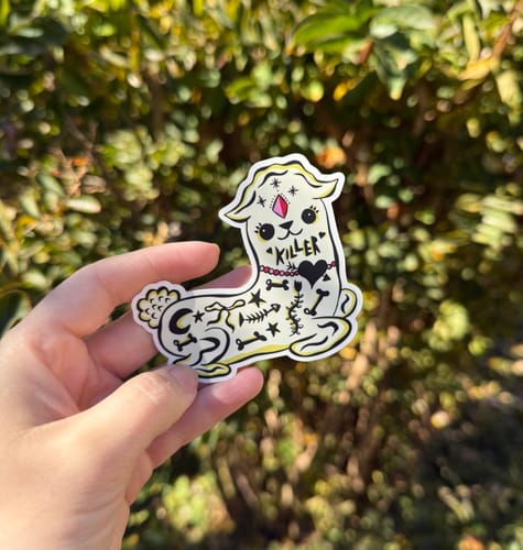 Customer's hand holding a custom vinyl sticker shaped like a light-colored alpaca with intricate black line art.