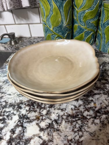 Customer's stack of cream stoneware Crema Deep Plates on a granite countertop.