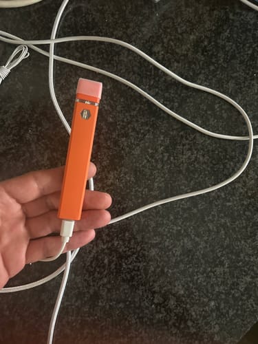 Customer's orange THC-A vape pen being charged with a white cable