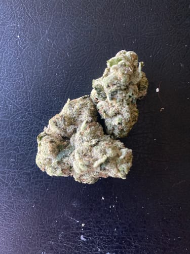 Customer's Blueberry THCA Flower, showing two dense and frosty green buds resting on a dark surface.