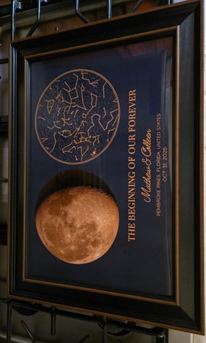 Customer's custom star map and moon phase poster framed in dark wood, displaying text and constellations.