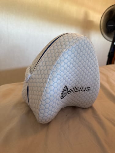 Customer's Cellsius orthopaedic knee pillow in white, featuring a honeycomb fabric texture and logo, placed on a bed.