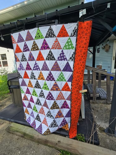 Customer's Spooky Summit quilt featuring colorful Halloween-themed triangles, hung outdoors on a wooden structure.