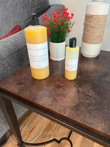 Customer's large and small Body Serum bottles on a dark side table next to a decorative plant.