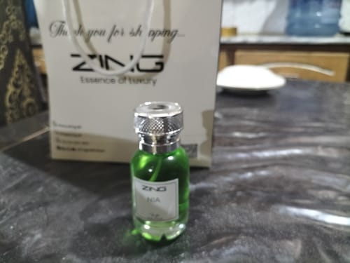 Customer's green glass bottle from the OUD Supreme Bundle with a silver cap, standing before a branded paper gift bag.