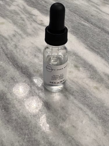 Customer's small clear glass bottle of Face Oil with a black dropper cap on a grey marble surface