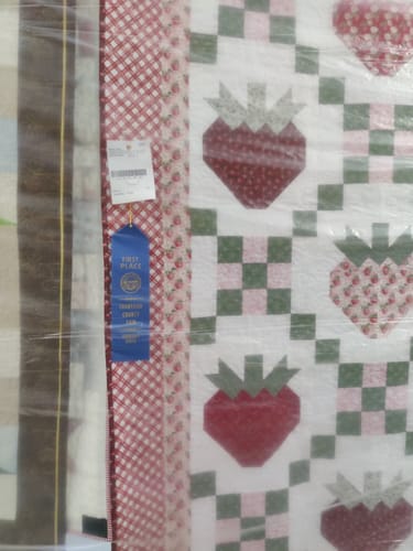 Reviewer's Strawberry Fields Sew-Ready Quilt Kit featuring red berry designs and a blue first-place fair ribbon.