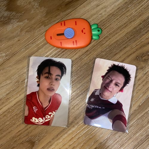 Customer's two CORTIS The 2nd EP GREENGREEN photocards lying on a wooden surface next to an orange carrot-shaped tool.