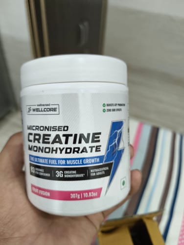 Customer's hand holding a white tub of Wellcore Micronised Creatine Monohydrate in a Fruit Fusion flavor.