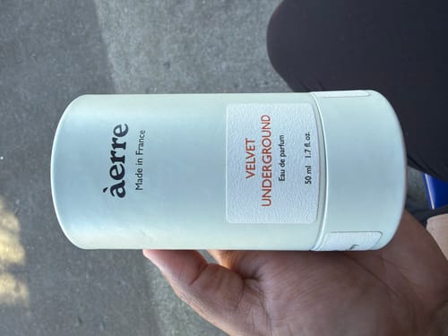 Reviewer's hand holding a cylindrical bottle of Aerre Velvet Underground perfume, featuring a light green label.