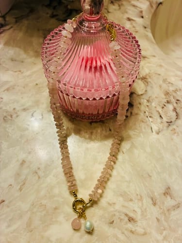 Customer's Rose Quartz Charm Necklace resting on a pink glass container on a marble countertop.