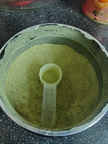 顧客的ProClean™狗狗天然潔牙護齒配方粉末，罐內附有一個淺色的量匙。