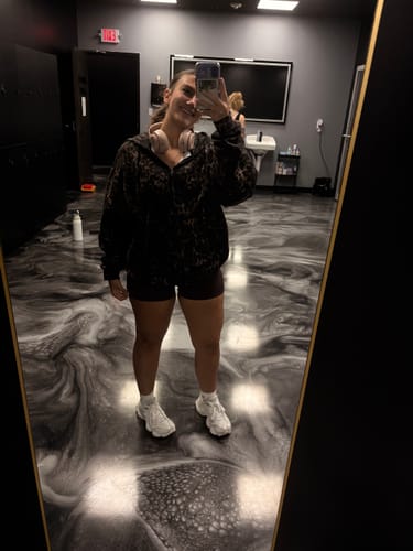 Customer's mirror selfie wearing an oversized black leopard print hoodie in a gym locker room.