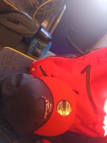 Customer's image taken on a bus, showing a black and red baseball cap on a seat next to a red backpack.