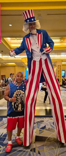 Customer wearing a blue 4th of July Calacas Basketball Jersey while standing next to a stilt walker in a costume.