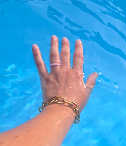Customer's gold J'adore Chunky Bracelet on a hand submerged in blue pool water.