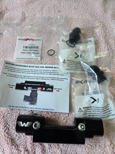 Customer's black billet fuel sensor mount, instruction sheet, and bagged fittings laid out on a soft surface.
