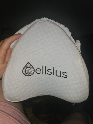 Customer's white, triangular Cellsius orthopedic knee pillow held in a hand