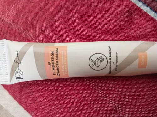 Customer's Advance Lip Pigmentation Cream tube lying on a textured red surface.