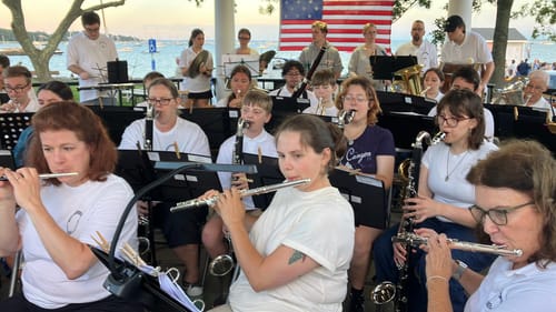 Customer's 15 Star American Flag displayed behind a town band performing outdoors at an evening concert.