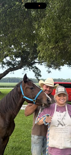 Reviewer's black bear T-shirt worn under an apron, standing outdoors with a horse and another person.