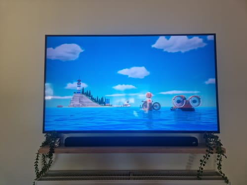 Customer's solid oak floating shelf holding a black soundbar under a television, decorated with trailing plants.