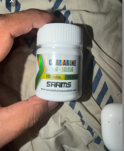 Customer's hand holding a white bottle of Cardarine tablets for post-cycle support.