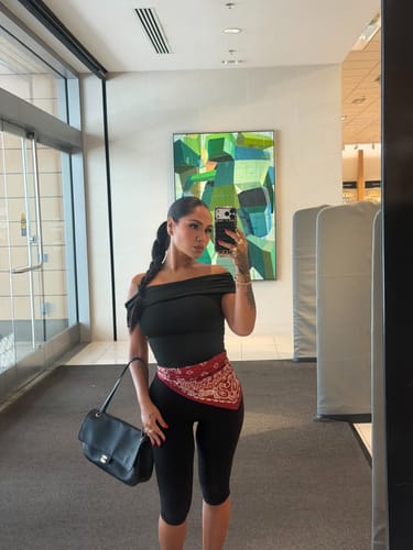 Reviewer wearing black Naked Capri Leggings, styled with a black top, a red bandana, and a shoulder bag.