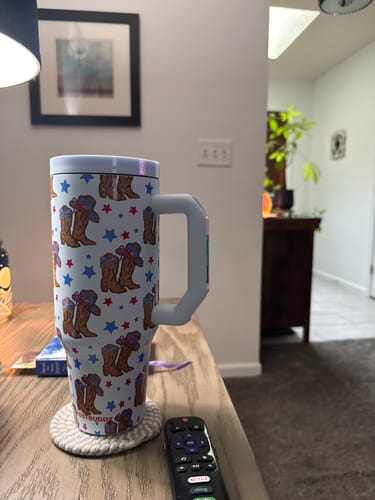 Customer's white Thicc Buddy mug with cowboy boot pattern and handle, resting on a coaster near a remote.