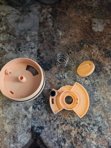 Customer's ONE Lid disassembled on a granite surface, showing the spring and internal components.