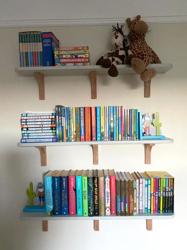 Customer's decorative oak wooden shelf brackets mounted on a wall, supporting three shelves filled with books.