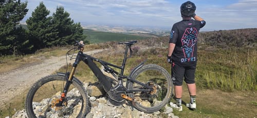 Reviewer standing on a trail looking at the view, wearing the black Invasion Flowteq Jersey with a neon graphic.