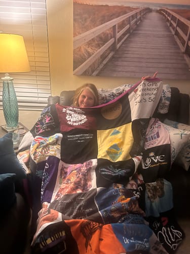 Customer's Project Repat T-Shirt Quilt held by a person on a couch in a living room.