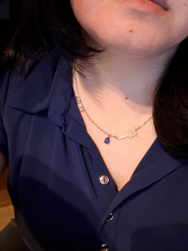 Customer's Lucce Signature Necklace with elegant script lettering and a blue teardrop stone worn around the neck.