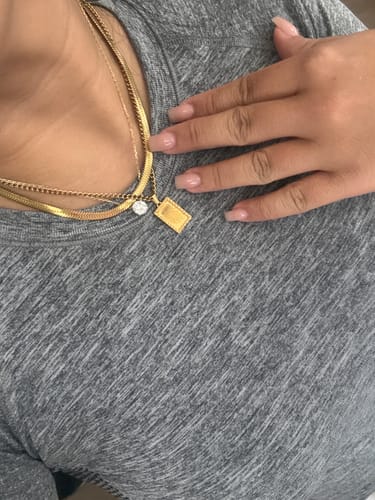 Customer's gold-tone Chelsea Herringbone necklace layered with other delicate chains on a person wearing a grey top.