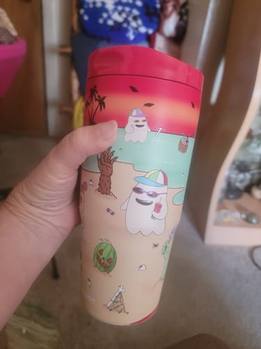 Customer's To-Go Buddy cup with ghost illustrations against a sunset background, held in a hand.
