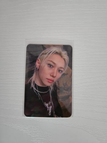 Customer's Stray Kids photocard featuring a blonde person in a black top with necklace, in protective sleeve.